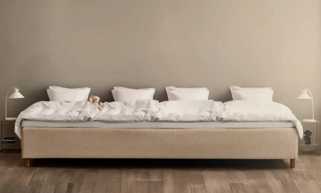 Ampio letto familiare beige rifatto con piumoni bianchi e quattro cuscini disposti in fila