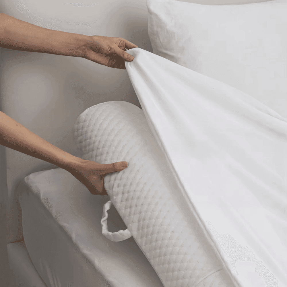 Mani che sistemano il lenzuolo bianco sopra un rullo in schiuma con finitura trapuntata lungo il bordo del letto