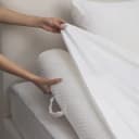 Mani che sistemano il lenzuolo bianco sopra un rullo in schiuma con finitura trapuntata lungo il bordo del letto