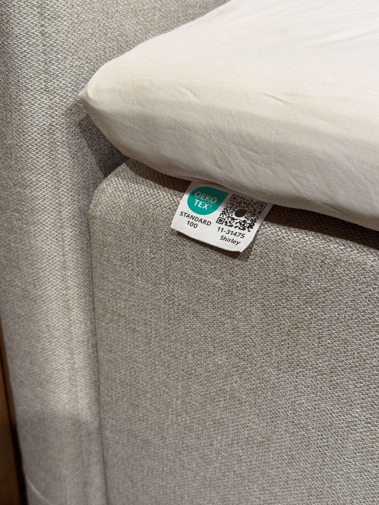 Etichetta OEKO-TEX® STANDARD 100 cucita sul tessuto beige del letto, sotto il lenzuolo