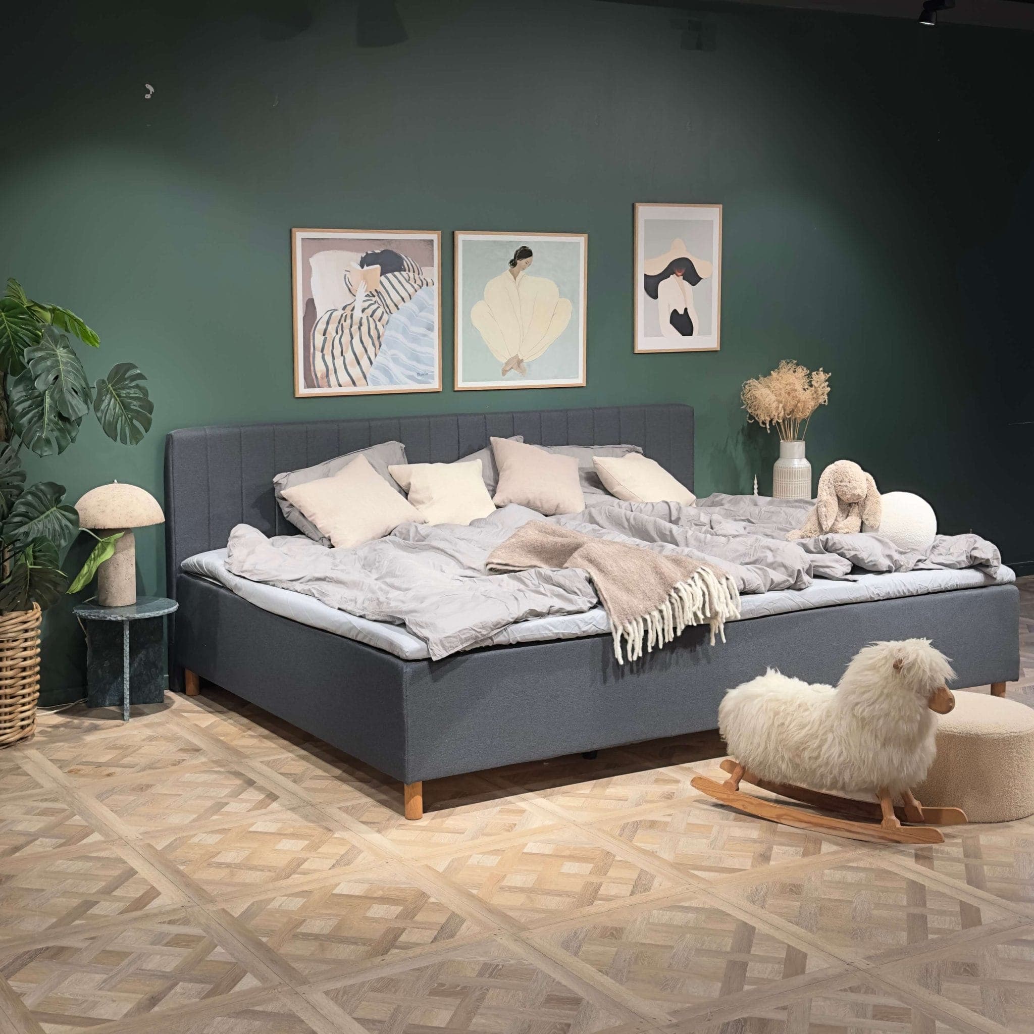 Ampio letto familiare grigio rifatto in una camera da letto con parete verde e una pecora a dondolo sul pavimento