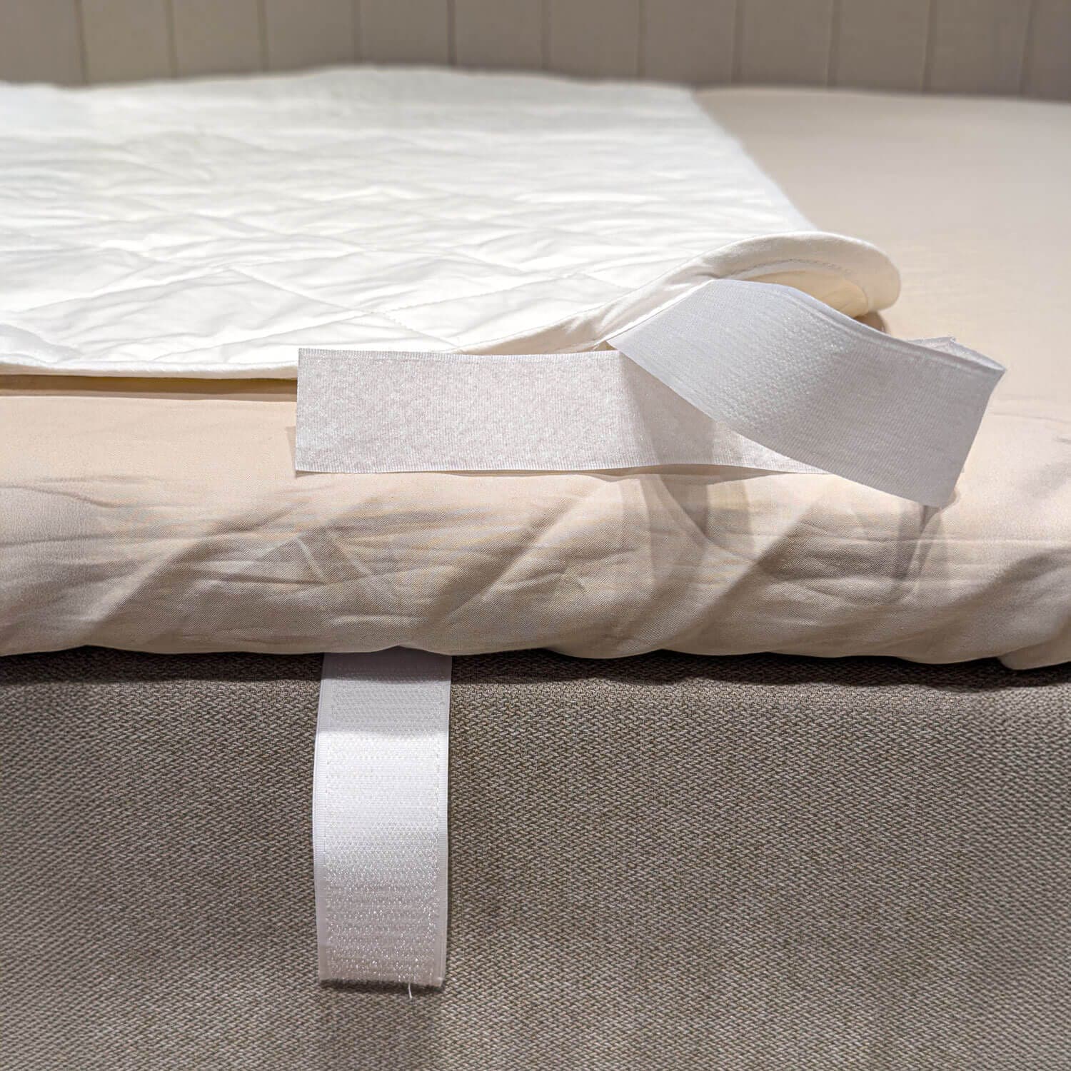 Angolo della protezione per materasso bianca e trapuntata, ripiegata per mostrare la fascetta in velcro attorno al bordo del letto