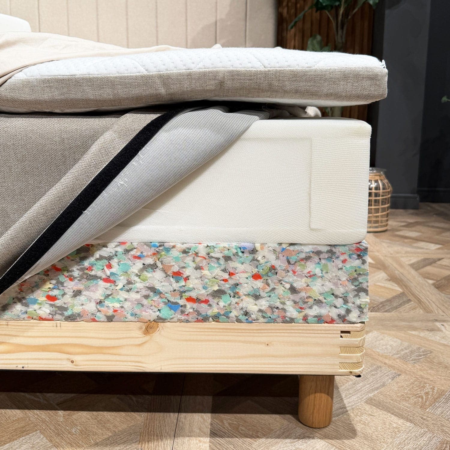 Angolo del letto con gli strati aperti: topper, materasso a molle con rivestimento aperto e bordo in schiuma della base sopra il telaio in legno