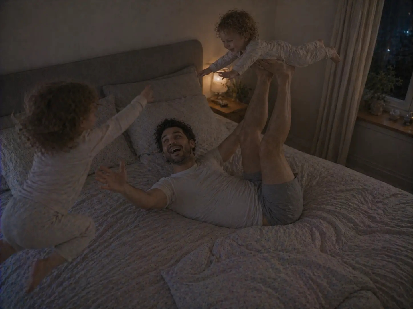 Un papà gioca all'aeroplano con uno dei figli sul letto, mentre l'altro salta accanto a loro