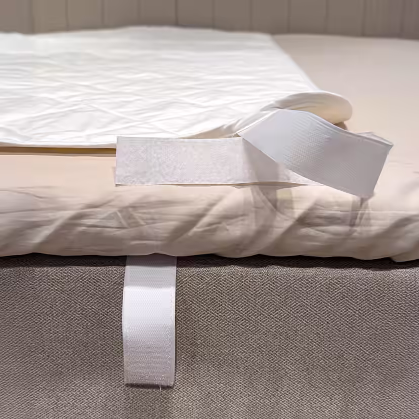 Angolo della protezione per materasso bianca e trapuntata, ripiegata per mostrare la fascetta in velcro attorno al bordo del letto