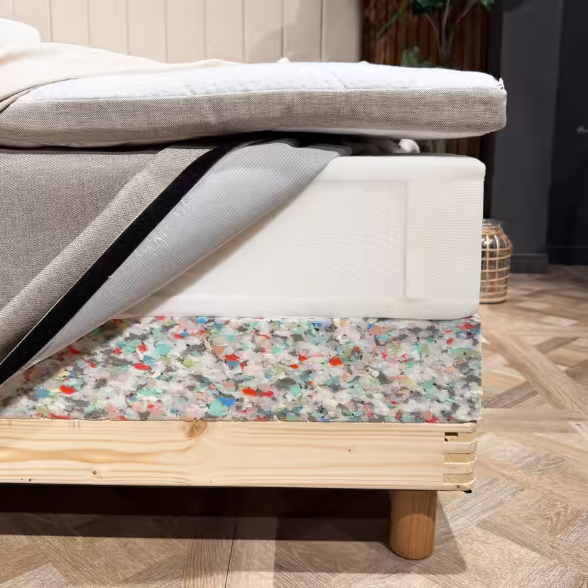 Angolo del letto con gli strati aperti: topper, materasso a molle con rivestimento aperto e bordo in schiuma della base sopra il telaio in legno